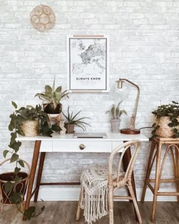 Chic boho hjemmekontor med retro træbord, boho tæppe, vægkunst, masser af stueplanter: kaktus og sukkulenter